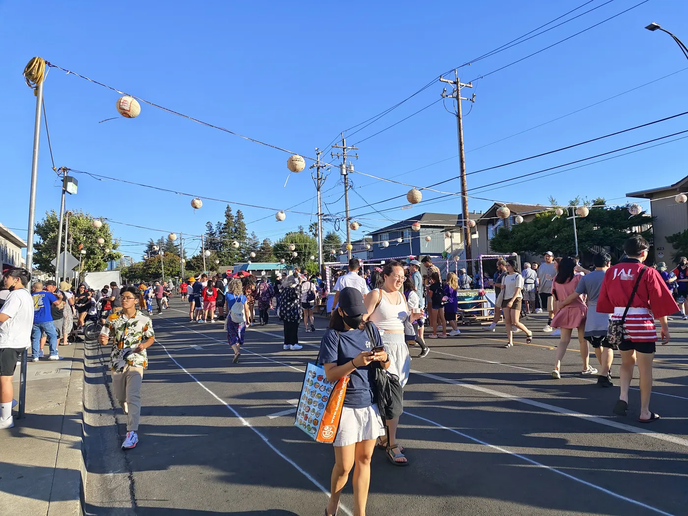 Paper lanterns strung over a crowded Jackson Street at golden hour during the Obon festival