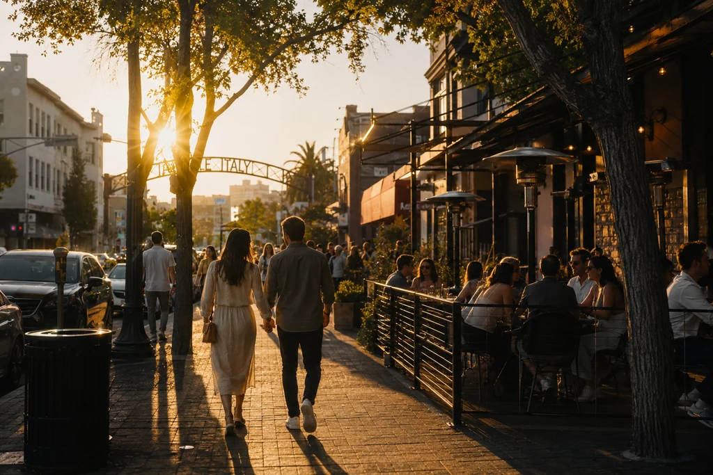 Couple walking past outdoor dining beneath the Little Italy gateway arch at golden hour.